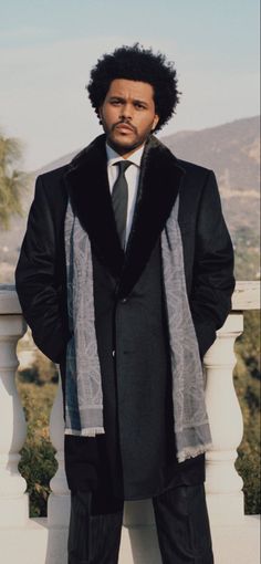 a man in a suit and tie standing on a balcony with his hands in his pockets