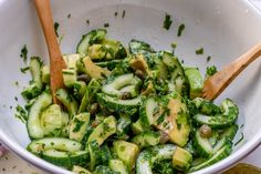 cucumber salad in a white bowl with two wooden spoons on the side