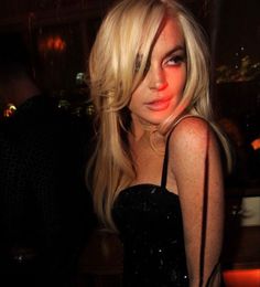 a woman with long blonde hair wearing a black dress and posing for the camera in a dimly lit room