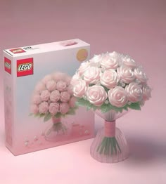 a bouquet of pink roses in a vase next to a box of legos on a pink background