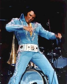 elvis presley performing on stage in blue outfit with gold trimmings and holding a microphone