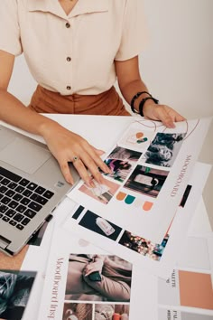 a woman sitting at a table working on a laptop computer surrounded by papers and photos