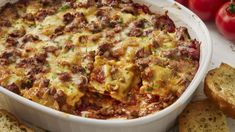 a casserole dish with meat and cheese in it next to bread on the table