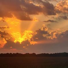 the sun is setting over an open field with trees in the distance and clouds in the sky