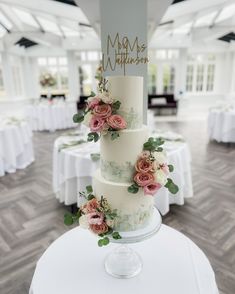 a three tiered wedding cake with pink flowers on the top and green leaves on the bottom