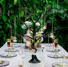 the table is set with wine glasses and an elegant tree centerpiece, along with other place settings