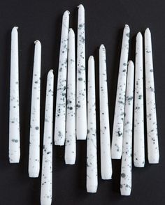 several white candles are lined up on a black surface with splattered paint all over them