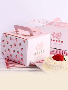 two pink boxes with strawberries on them sitting next to a white plate and cake