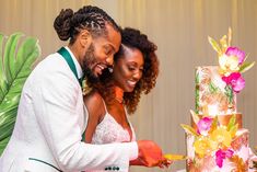 a man and woman cutting into a cake with flowers on the table next to them