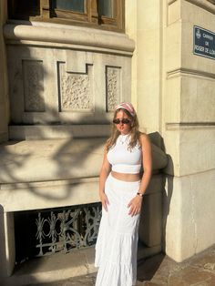 a woman standing in front of a building wearing a white skirt and cropped top