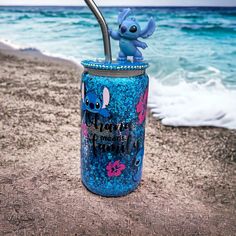 a blue cup with a straw in it sitting on the beach