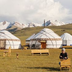 two people sitting on benches in front of yurts with snow capped mountains in the background