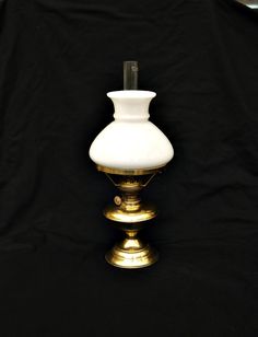 a white vase sitting on top of a metal stand next to a black backdrop with gold trim