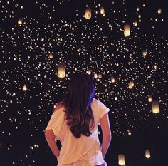 a woman standing in front of a sky full of lit up paper lanterns at night