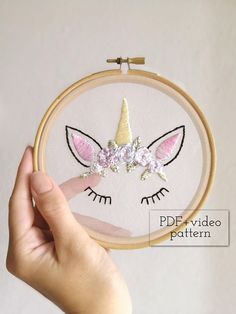 a hand is holding up a embroidery hoop with an embroidered unicorn's face