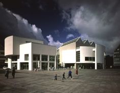 people are walking around in front of a large white building with many windows on it