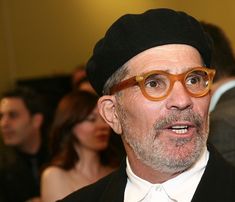 a man wearing glasses and a black hat is talking to someone in the audience at an event