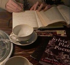 a person sitting at a table reading a book and holding a coffee cup with both hands