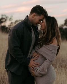 a pregnant couple cuddle in the middle of a field at sunset during their newborn photo session