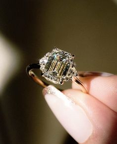 a close up of a person's hand holding a ring with a diamond in it