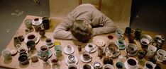 a woman is sitting at a table covered in cups and saucers with her head down