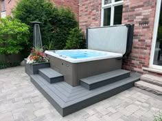 a large hot tub sitting on top of a patio next to a brick building and flowers