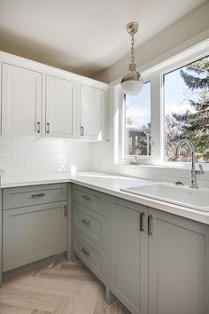 a kitchen with gray cabinets and white counter tops, along with a large window that looks out onto the outdoors