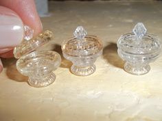 three small glass containers sitting on top of a table next to a person's hand