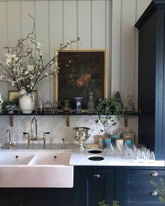 a kitchen with marble counter tops and blue cabinets, white flowers in vases on the shelf