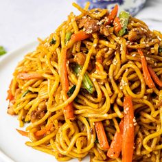 a white plate topped with noodles and vegetables next to chopsticks on a table