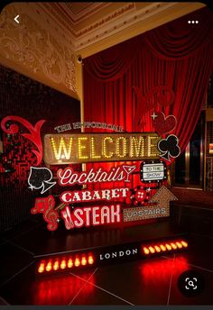 a welcome sign is lit up in front of a red drapeed curtain and floor