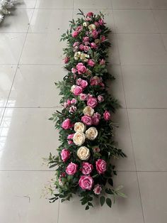 an arrangement of pink and white roses on the floor in a long line with greenery