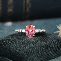 an oval shaped pink sapphire and diamond ring on top of a black velvet cushion with a book in the background