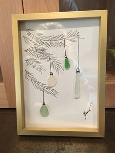 a frame with some glass ornaments hanging from it's sides and pine needles on the other side