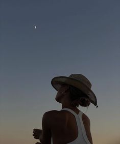 a woman wearing a hat looking up at the moon