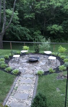 a fire pit in the middle of a yard with chairs and tables around it, surrounded by trees