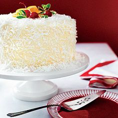 a white cake with coconut and cherries on top sitting on a table next to plates