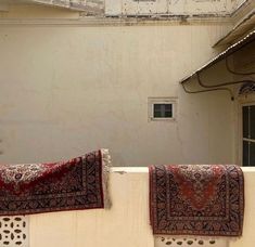 two red and black rugs hanging on a white wall next to a doorway with a window