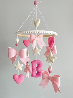 a pink and white mobile with hearts, stars, and bows hanging from the ceiling