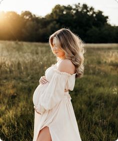 a pregnant woman standing in a field with her legs crossed and wearing a white dress