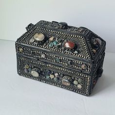 an ornate black box with stones and beads on the lid sits on a white surface