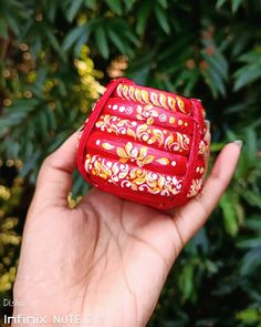 a hand holding a small red case with flowers on it