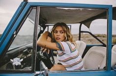 a woman sitting in the driver's seat of a blue truck with her hand on the steering wheel