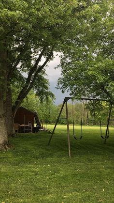 a swing set in the middle of a grassy field next to a tree with a barn in the background