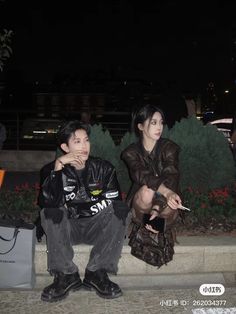 a man and woman sitting on the ground next to each other with bags in front of them