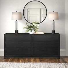 a black dresser with two lamps and a round mirror on the wall above it, along with a white rug