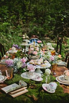 an outdoor table set up for a tea party in the woods with flowers and greenery