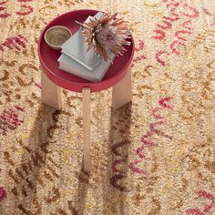 a red table topped with books and a vase filled with flowers on top of a rug