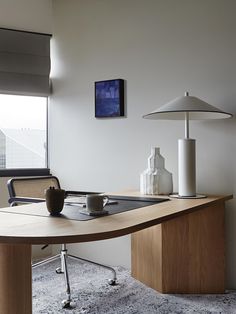 a desk with a lamp and vase on it in front of a window overlooking the city