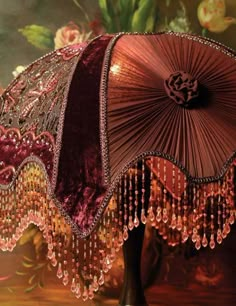 an umbrella with beads hanging from it's side on a stand in front of a painting